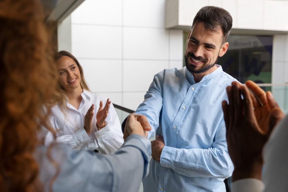 Dos personas se aprietan las manos en un ámbito laboral mientras los demás aplauden