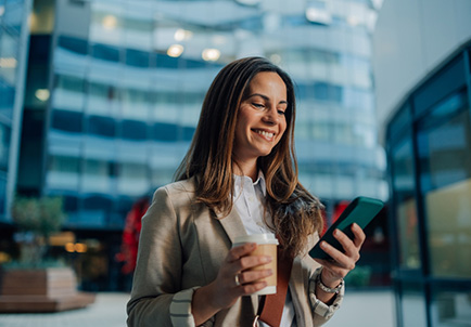 Mujer de negocios caminando en ciudad mientras usa smartphone y sostiene café