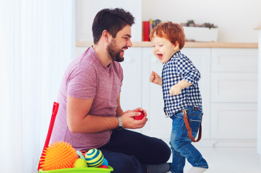Padre e hijo compartiendo una manzana en casa mientras juegan con juguetes educativos en el suelo