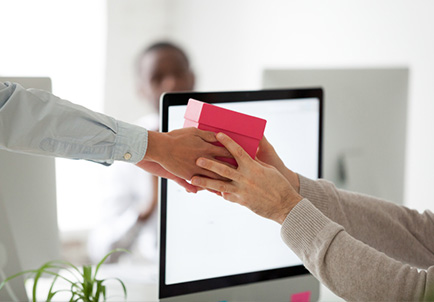 Mano entregando un regalo a otra persona frente a ordenador