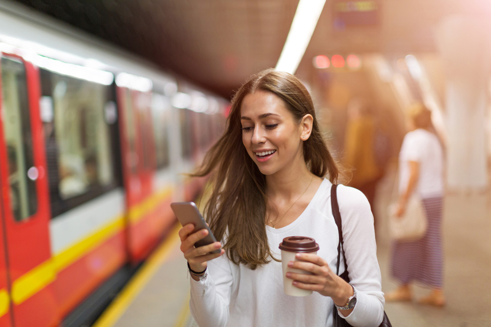 Mujer con café usando teléfono móvil en estación de metro