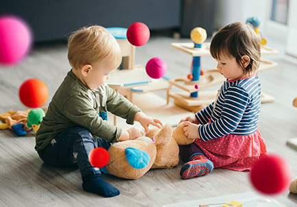 dos niños juegan con un tren de juguete sobre el suelo, en una habitación colorida y luminosa