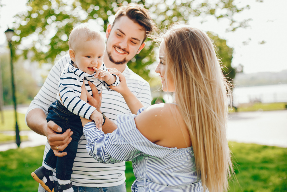 Padre y madre jugando con su bebé al aire libre en un parque soleado. Maternidad y paternidad en familia.